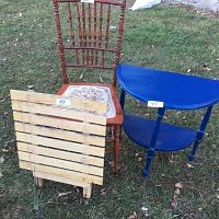 Whole lot showing wood chair with embroidered seat, blue half moon wood table, and outdoor wood slat table.