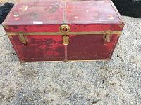 Front and top view of a red storage trunk with metal accents showing wear and locks on front.