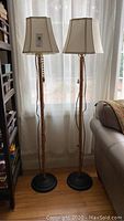 Two full view bamboo-style floor lamps with cream fabric shades beside a window and sofa.