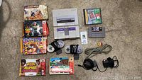 All items included in the lot visible on a carpeted floor: SNES console, six SNES game cartridges, two controllers, cables, and memory card.
