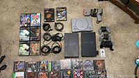 Overview of two PS2 slim consoles, one PS1 console, controllers, light gun, cables and game cases laid out on floor
