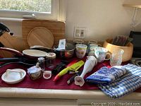 Photo showing immersion blender, owl mugs, skillets, kitchen utensils, wooden salad bowl, cutting boards, table linen and oven mitt on kitchen counter.