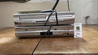 Two DVD players stacked, top labeled Sylvania with a remote on top, and bottom labeled Samsung