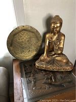 Front view of gilded wooden Buddha statue seated next to round brass platter