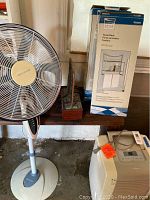 Photo of white standing fan, shelf towel rack boxes, and desktop water feature on wooden base.