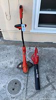 Black & Decker orange weed whacker with curved shaft alongside a Homelite leaf blower