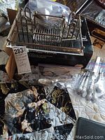 Photo of the silver plated flatware caddy with visible discoloration and multiple bags of flatware pieces around it on a quilted surface.
