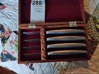 Top-down photo of one wooden box containing 4 Gerber steak knives with metal handles and blades on fabric background.