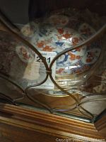 Plates stacked inside a wooden cabinet behind diamond-patterned glass, visible floral and geometric details on top plate