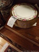 Stack of twelve white charger plates showing pink floral inner ring and wide gold outer rim