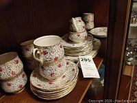Photo showing stacked bone china tea cups and saucers with golden and rose pattern on a wooden shelf