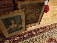 Image showing two framed lithographs leaning against a wall on a detailed patterned carpet, with the left one depicting a woman in blue.