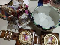 Porcelain figurines of an 18th-century styled man and woman, ceramic bowl with ruffled edges and floral decorations, and vintage leather belt with two porcelain medallions.