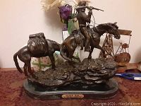 Front view of entire sculpture showing cowboy on horseback and pack horse on rocky base