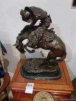 Full view of bronze sculpture depicting cowboy on bucking horse with rattlesnake under neck on marble base