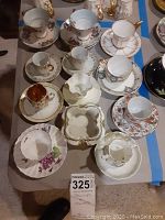Overview of 11 teacups, 13 saucers, and one decorative dish with various floral patterns and gold detailing.