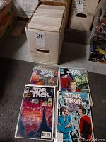 Photo showing a cardboard box filled with comics and four Star Trek comics displayed outside the box.