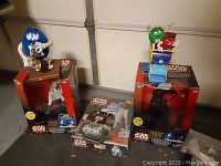 Photo showing the various Star Wars episode 1 talking banks and M&M banks in their original packaging with the blue M&M saxophone figure prominently.