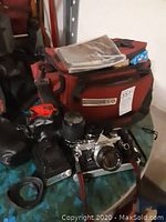 Olympus OM-1 camera body with lenses and red camera bag with paperwork on top, showing lot contents and condition.