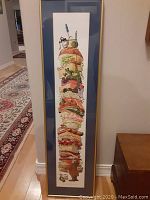 Full view of the tall framed artwork depicting a colorful sandwich stack with cartoon animals