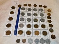 Photo showing a collection of over 40 Canadiana tokens arranged in rows, some in protective sleeves with handwritten labels, rulers for scale, both brown and silver-colored tokens.