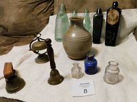 Wide view of all lot items on table showing antique bottles, inkwells, bells and crock.