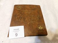 Closed brown Uni-Safe coin folder with gold embossed U.S. map and text on cover, showing the 50 Washington quarters inside.