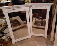 Front view of two white wood framed mirrors side by side showing rectangular shape with crown molding on top and arch design on mirror glass.