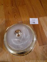 Photo of one gold-tone flushmount light fixture with glass cover on wooden floor, showing ribbed swirl swirl glass pattern and central gold-tone knob.