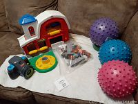 Fisher Price barn set with animals and farmer, three textured balls, and Playskool camera on couch.