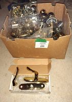 Photo of large cardboard box filled with multiple used doorknobs and hardware items, mostly gold-colored with some silver-tone, showing overall quantity and condition.