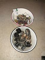 Overhead photo showing two white enamel pans; one with assorted cabinet knobs in gold and ceramic, the other with mixed plastic and metal wheels.