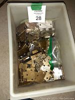 White container filled with assorted used cabinet hinges of various sizes and types, including some small screws and packages.