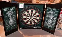 Front view of dart board cabinet open, showing dart board and chalk scoreboards on doors.