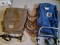 Two vintage hiking backpacks with rigid aluminum frames, one brown and one blue, positioned around ten horseshoes on the floor.