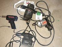 Top view of the four power tools grouped on the floor, showing cords and labels, including the drill with repaired cord.