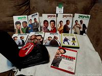 Photo shows all 8 seasons of Psych TV series in DVD cases with cover art, plus Psych: The Musical DVD case, and Monk seasons 1-7 DVDs stored in a black zippered Case Logic disc folder.