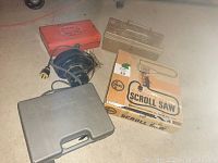 Photo showing closed boxes including red and plastic gray case, cord reel, and scroll saw box