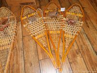 Five Torpedo wooden snowshoes with rawhide webbing and leather bindings laid out on wood floor