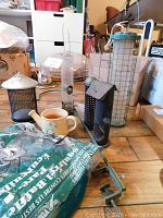 Photo showing various bird feeders, metal deck hanger, and flower pots on a wooden table.