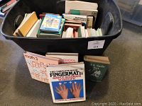 Plastic bin filled with various teacher resource books including math and phonics materials with some titles shown outside the bin.