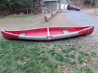 Side view of red canoe on grass showing interior seats, yoke and overall shape
