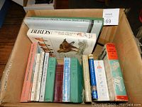 Box of assorted non-fiction books primarily about nature, birds, trees, anatomy, and wildlife. Visible book titles include North American Birds of Prey, Birds Throughout the World, Native Trees of Canada, and a home carpentry handbook.