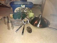 Photo showing the entire lot including stainless steel wok with lid, ladles, pewter cups, green glass cups, pepper grinder, and possible lead dish.