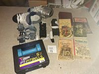 Photo showing the black carrying case with two blue 5lb weights, two sets of double blade learning skates, adult size 4 skates, and four assorted vintage books.