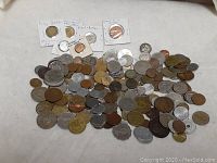 Top view of over 200 assorted world coins spread on a surface, showing various sizes, colors, and conditions.