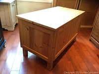 Rectangular pine blanket box with visible wood grain and natural finish, standing on four legs on wooden floor.