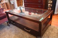 Overall view of rectangular dark wood coffee table with glass top insert, showing legs, lower shelf and two drawers.
