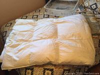 Folded white feather duvet on patterned bedspread.