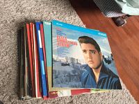 Stack of vinyl records with the top album being 'Elvis' Christmas Album' showing cover artwork of Elvis Presley in blue coat with snowy background.